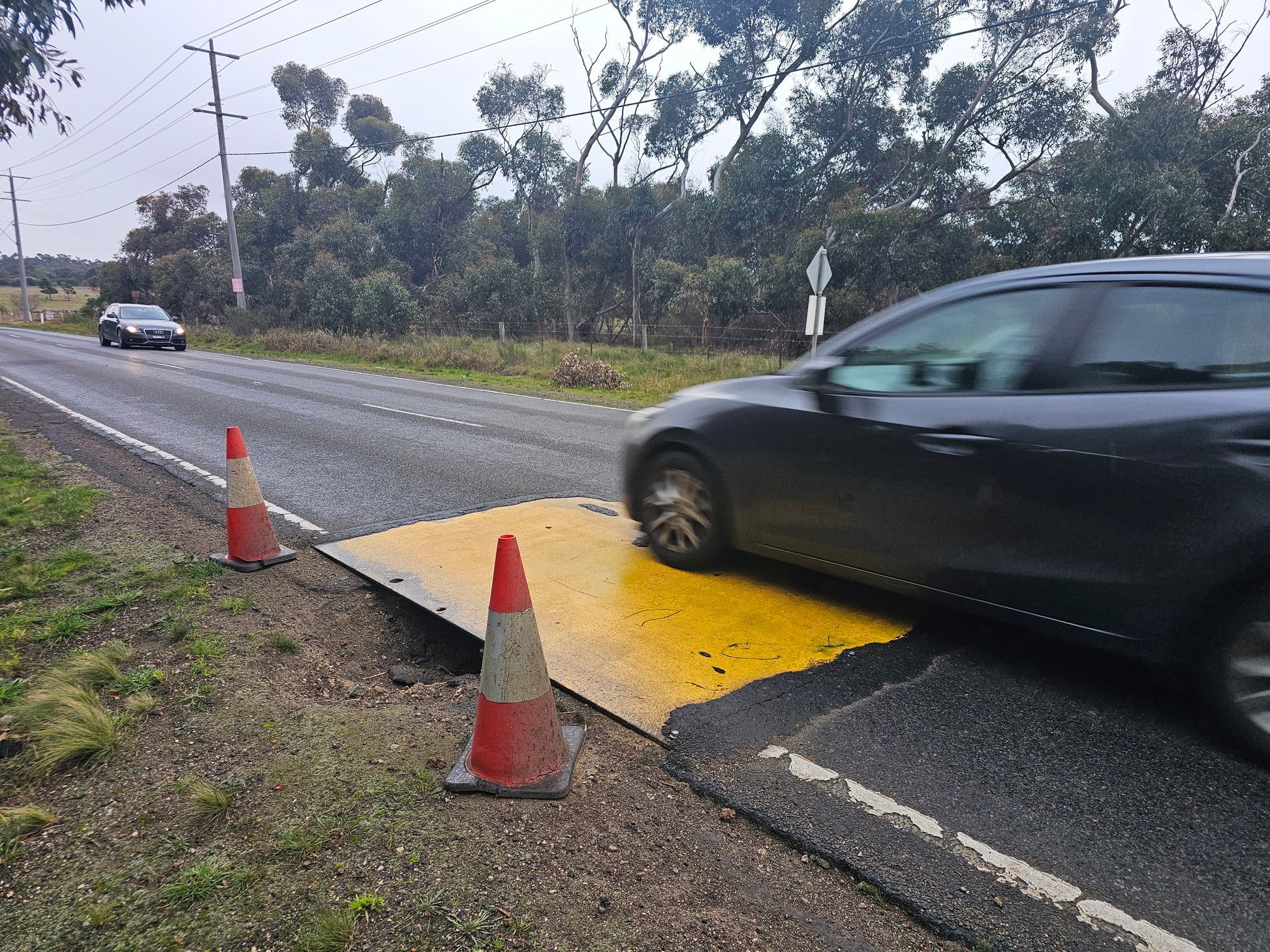 Yellow anti-slip coated RAPTA road plate carrying live traffic over a road excavation
