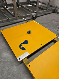 Yellow anti-slip coated RAPTA steel road plates laid out on a workshop floor. Shown with optional lifter. Custom sizes available. 
