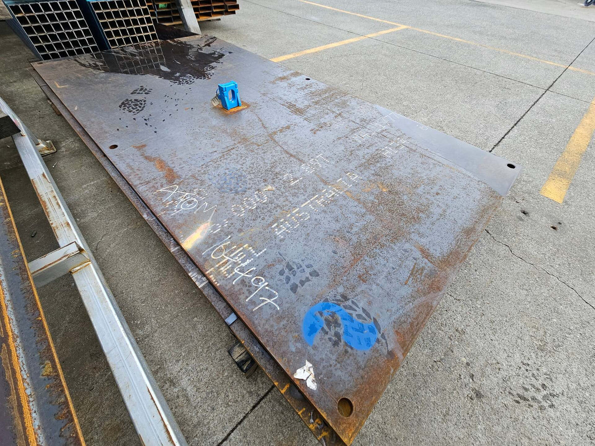 Yellow heavy duty steel road plate with a lifter and multiple fixing holes, placed on a concrete surface.