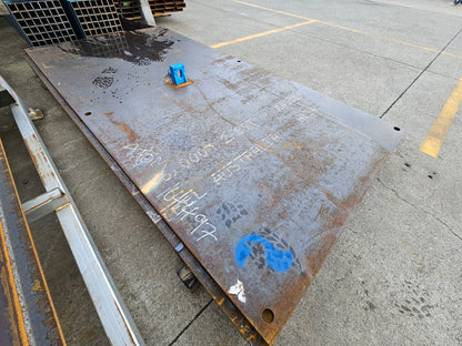 Yellow heavy duty steel road plate with a lifter and multiple fixing holes, placed on a concrete surface.