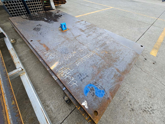 Yellow heavy duty steel road plate with a lifter and multiple fixing holes, placed on a concrete surface.